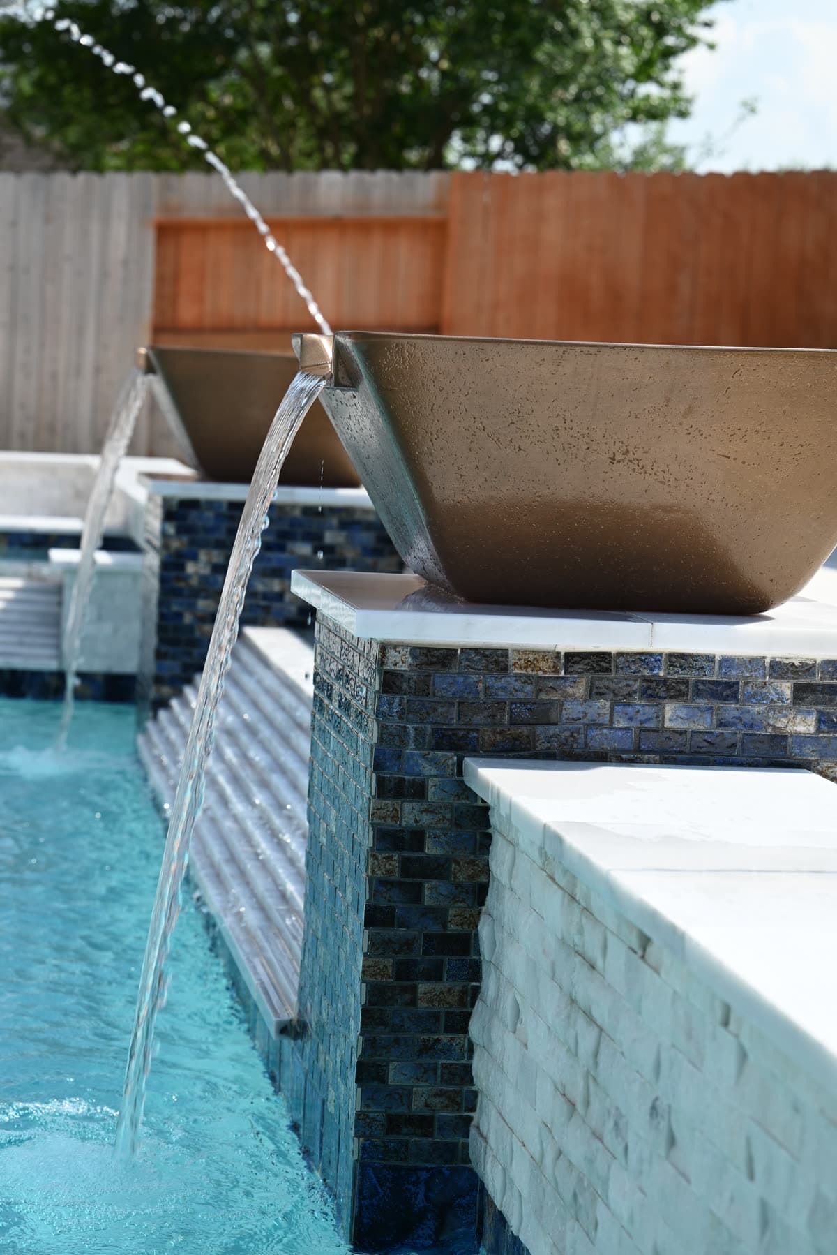 Custom pool in the Houston area. Two bronze bowls pouring arcs of water over blue glass mosaic into turquoise water.