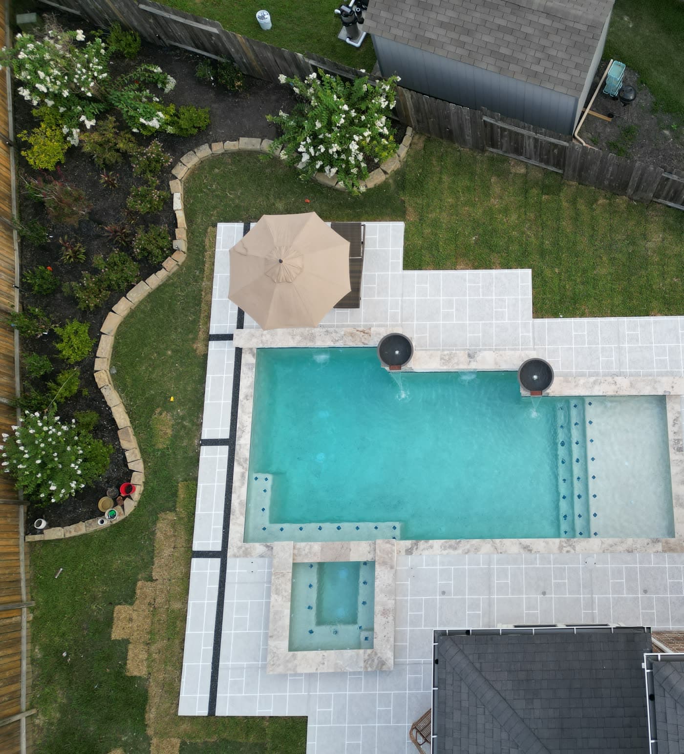 Custom pool in Spring, TX. Seen from above at golden hour: two fire bowls on pedestals, a raised spa, a tanning ledge and a sheet of water spilling into the pool.