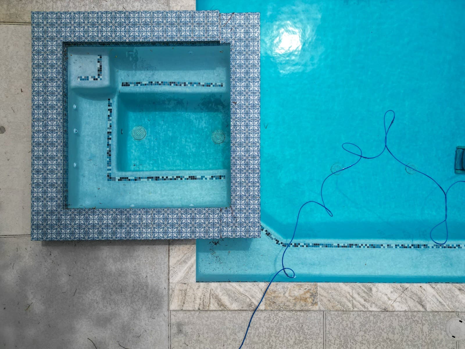 Custom pool in The Woodlands, TX. Straight down onto the square spa in blue-and-white patterned tile, a mosaic band tracing its bench and the pool's tile line beside it.