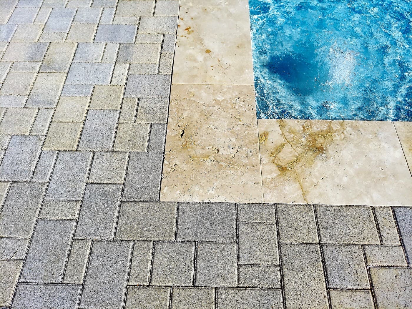Custom pool in The Woodlands, TX. Close detail where the grey paver deck meets the light stone coping at the pool's corner, the water rippling beside it.